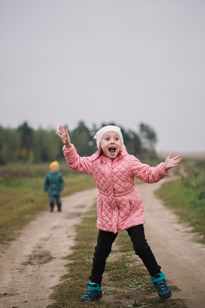 Kleines kaukasisches Mädchen, das mit ihrem Bruder auf dem Feld läuft und lustige Gesichter macht.