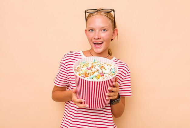 Kleines kaukasisches Mädchen, das Popcorn isst, isoliert auf beigem Hintergrund