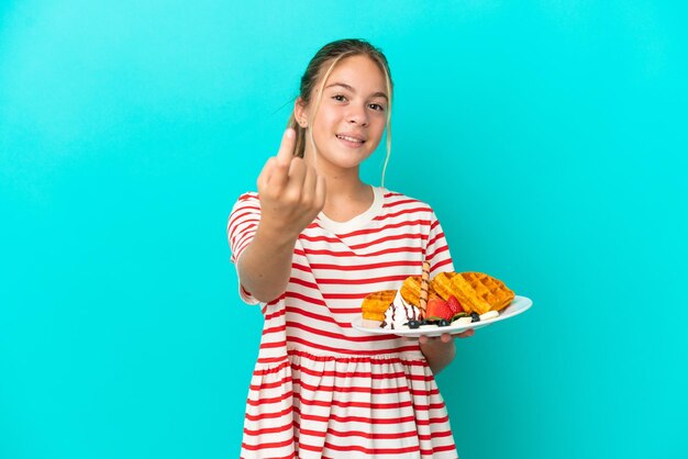 Kleines kaukasisches Mädchen, das Waffeln isoliert auf blauem Hintergrund hält und eine kommende Geste macht