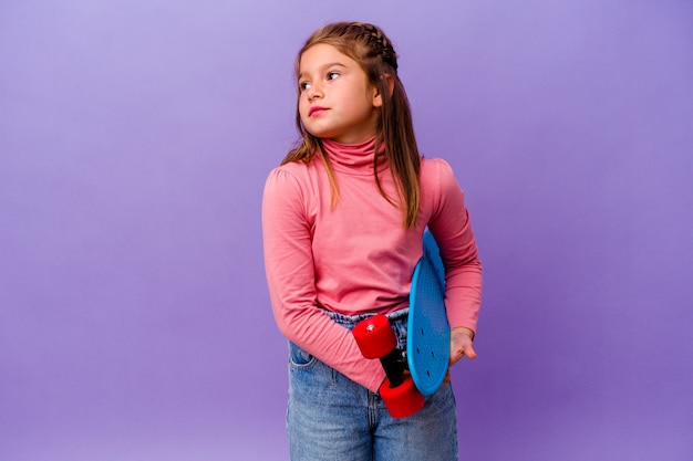 Kleines kaukasisches Mädchen des Skaters lokalisiert auf der blauen Wand, die vom Erreichen von Zielen und Zwecken träumt