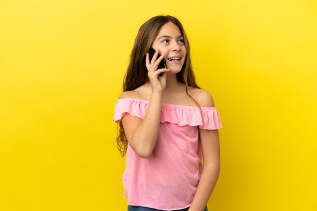 Kleines kaukasisches Mädchen isoliert auf gelbem Hintergrund, das ein Gespräch mit dem Handy führt