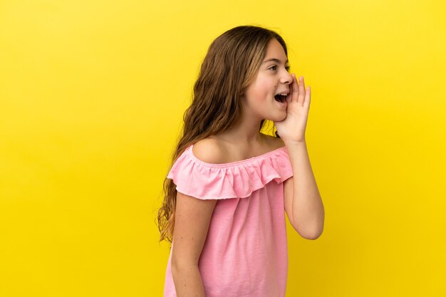 Kleines kaukasisches Mädchen isoliert auf gelbem Hintergrund, das mit weit geöffnetem Mund zur Seite schreit