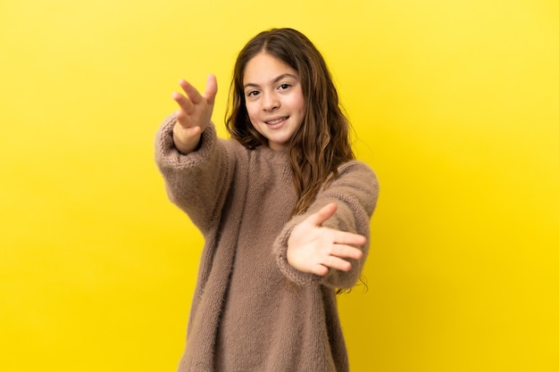 Kleines kaukasisches Mädchen isoliert auf gelbem Hintergrund, das präsentiert und einlädt, mit der Hand zu kommen