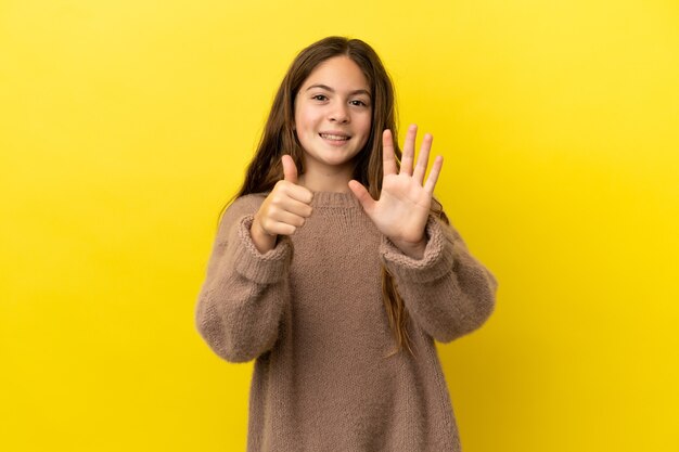 Kleines kaukasisches Mädchen isoliert auf gelbem Hintergrund, das sechs mit den Fingern zählt