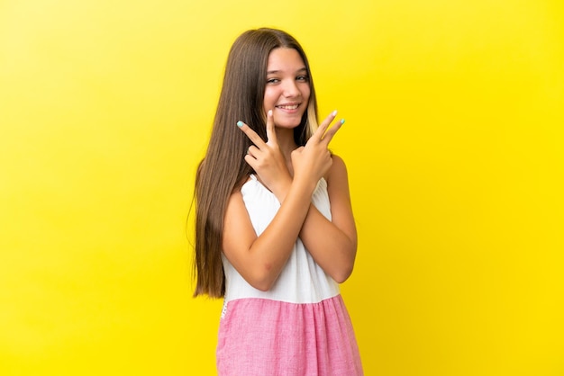 Kleines kaukasisches Mädchen isoliert auf gelbem Hintergrund, das Siegeszeichen lächelt und zeigt