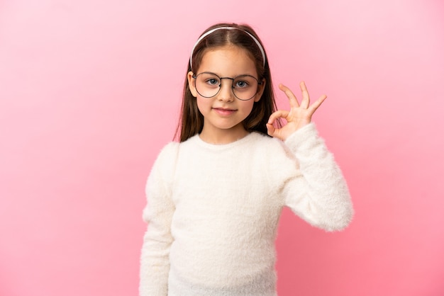 Kleines kaukasisches Mädchen isoliert auf rosa Hintergrund, das ein Okay-Zeichen mit den Fingern zeigt