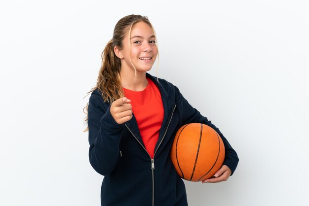 Kleines kaukasisches Mädchen isoliert auf weißem Hintergrund, das Basketball spielt und nach vorne zeigt