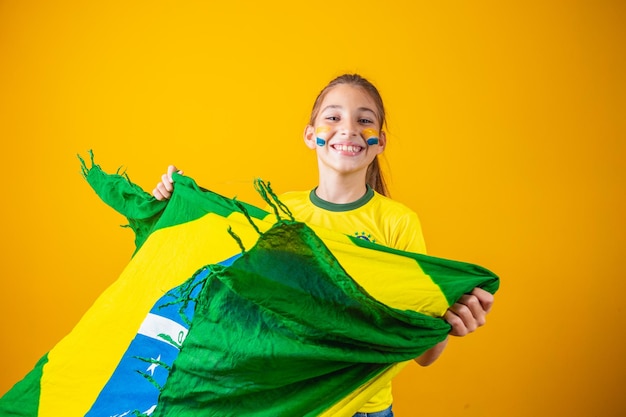 Kleines kaukasisches Mädchen mit Brasilien-Flagge auf gelbem Hintergrund. Brasilianischer Kinderbetreuer