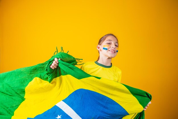 Kleines kaukasisches Mädchen mit Brasilien-Flagge auf gelbem Hintergrund. Brasilianischer Kinderbetreuer