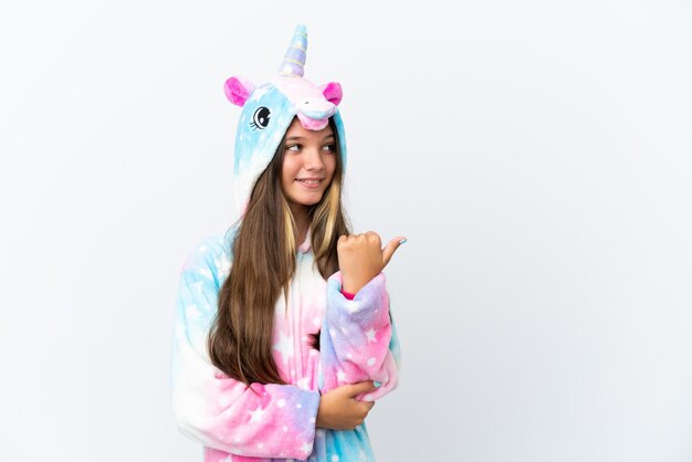 Kleines kaukasisches Mädchen mit Einhorn-Pyjama isoliert auf weißem Hintergrund, das auf die Seite zeigt, um ein Produkt zu präsentieren