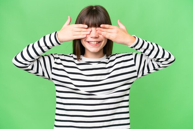 Kleines kaukasisches Mädchen mit isoliertem Hintergrund, das die Augen mit den Händen bedeckt und lächelt