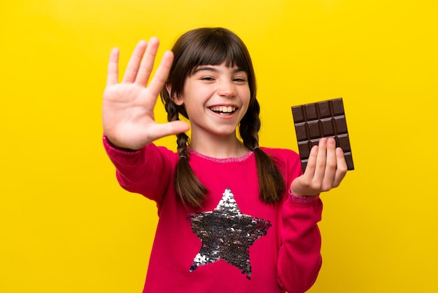 Kleines kaukasisches Mädchen mit Schokolade isoliert auf gelbem Hintergrund, das fünf mit den Fingern zählt