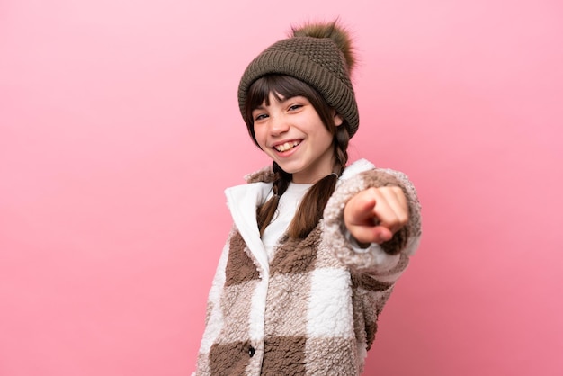 Kleines kaukasisches Mädchen mit Winterjacke isoliert auf rosa Hintergrund zeigt mit einem selbstbewussten Ausdruck mit dem Finger auf dich