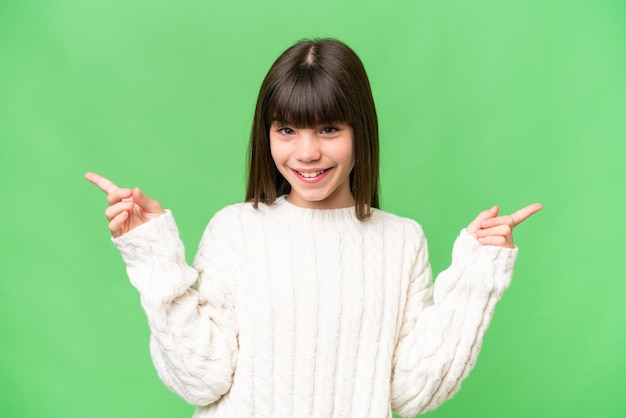 Kleines kaukasisches Mädchen über isoliertem Hintergrund, das mit dem Finger auf die Seitenteile zeigt und glücklich ist