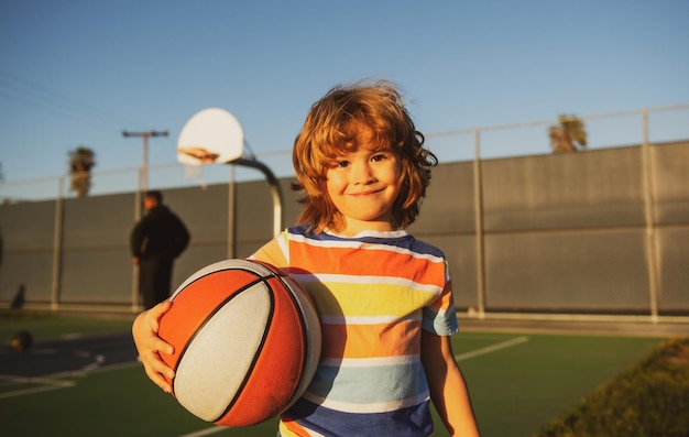 Kleines kaukasisches Sportkind, das Basketball spielt und Ball mit glücklichem Gesicht hält