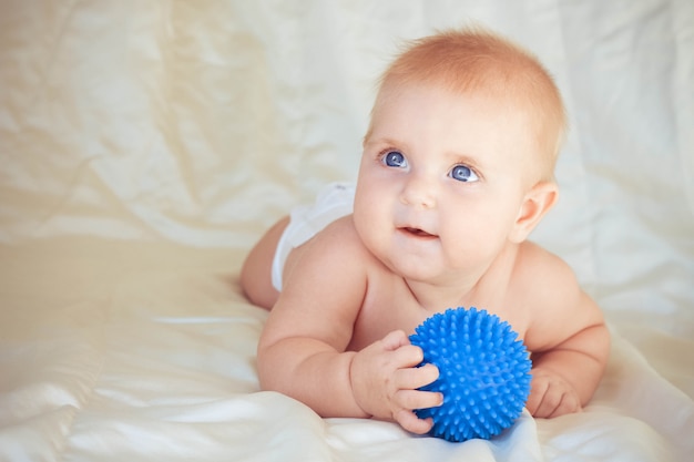 kleines Kind auf dem Bauch liegend und Ball zur Massage haltend