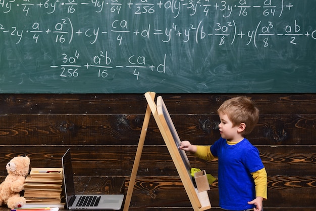 Kleines Kind, das an Tafel schreibt. Kind vor Brett mit mathematischer Gleichung. Kluger Schüler, der Mathematik studiert