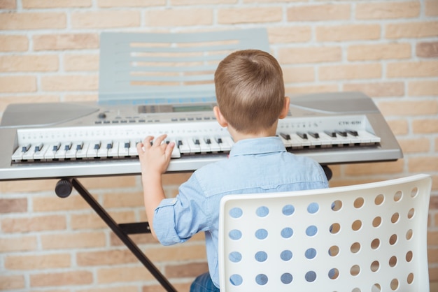Kleines Kind, das E-Piano während der Musiksitzung in der Akademie übt