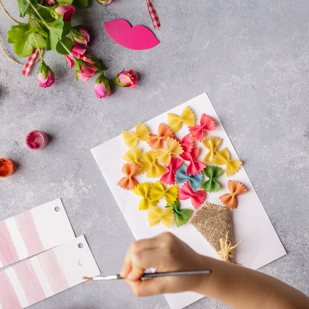Kleines Kind, das einen Blumenstrauß aus farbigem Papier und farbigen Teigwaren heraus tut.
