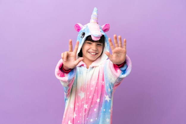 Kleines Kind, das einen Einhornpyjama trägt, der auf violettem Hintergrund isoliert ist und acht mit den Fingern zählt