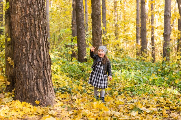 Kleines Kind, das im Herbstpark geht und gelbe Blätter hält