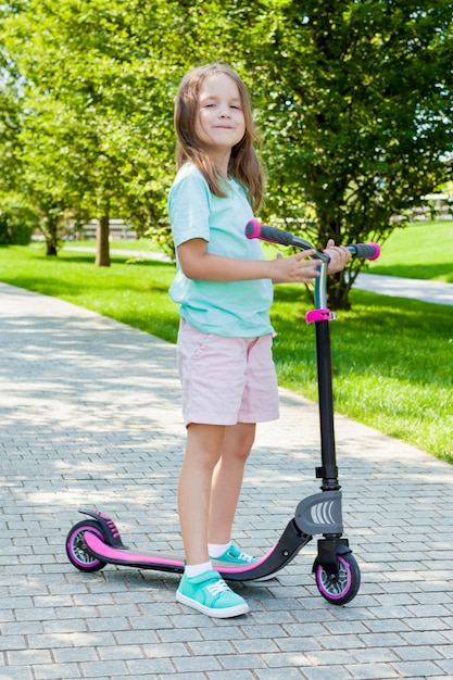 Kleines Kind, das lernt, einen Roller in einem Stadtpark am sonnigen Sommertag zu reiten. Aktive gesunde Freizeit und Outdoor-Sport für Kinder.