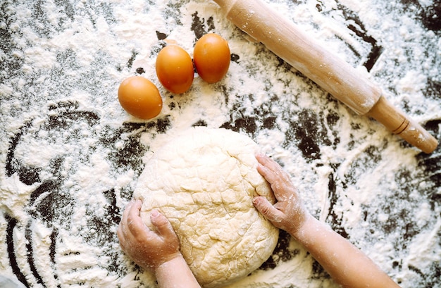 Kleines Kind, das Teig zum Backen zubereitet. Kleine Hände kneten Teig und gerollten Teig