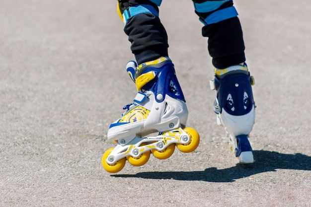 Kleines Kind fährt auf blau-gelben und weißen Rollschuhen Schnappschuss eines Kindes, das Rollerblade lernt