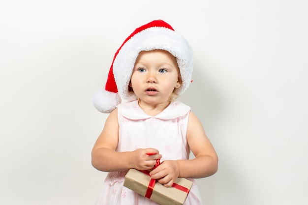 Kleines Kind in einem Hut von Santa Claus hält ein Geschenk auf hellem Hintergrund. Banner. Geschenkkonzept für Weihnachten und Winterferien, glückliche Familie.