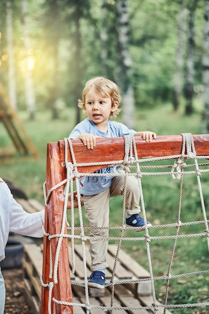Kleines Kind klettert mit Seilen im grünen Park auf ein Hindernis