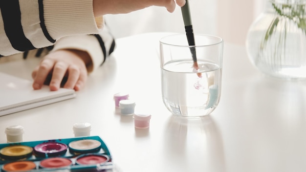 Kleines Kind Mädchen Künstler waschen Pinsel im Glas Wasser Zeichnung Malbild mit Farben