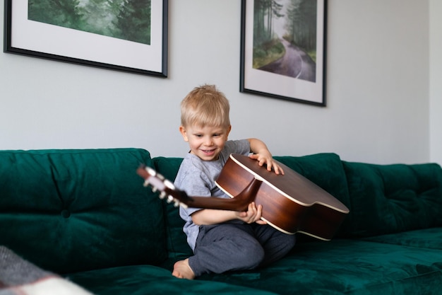 Kleines Kind mit blonden Haaren, das zu Hause Gitarre spielt