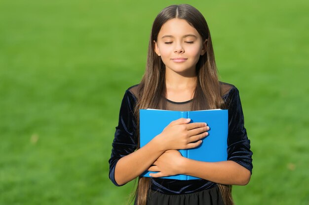 Kleines Kind mit geschlossenen Augen hält Schulbuch grünes Gras Sommer im Freien Wissen