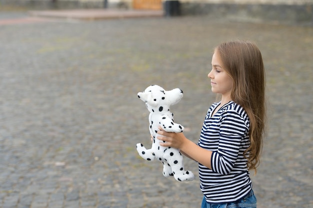 Kleines Kind mit langen Haaren im lässigen Modestil spielt mit Spielzeughund im Freien im Kopierraum