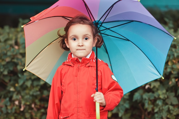 Kleines Kind mit mehrfarbigem Regenbogenregenschirm draußen.