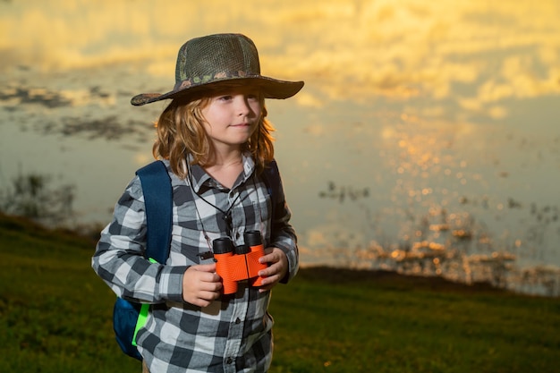 Kleines Kind mit Rucksack und Fernglas Fantasie oder Erforschung im Park Glückliches Kind spielt mit Fernglas Junger Touristenforscher Kinderurlaub und Reisen Sommerreise für Kinder