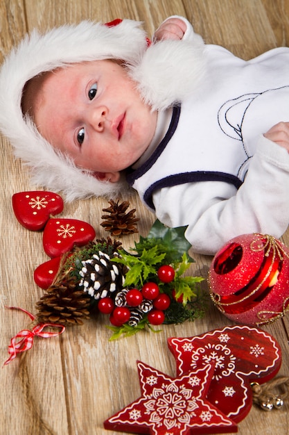 Kleines Kind mit Weihnachtshut auf Holz mit Weihnachtsdekoration