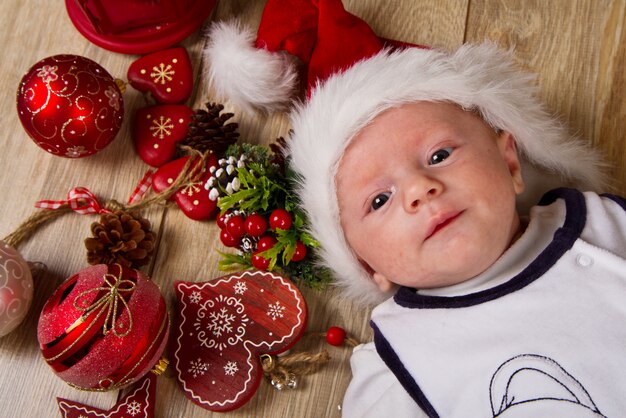 Kleines Kind mit Weihnachtshut auf Holz mit Weihnachtsdekoration