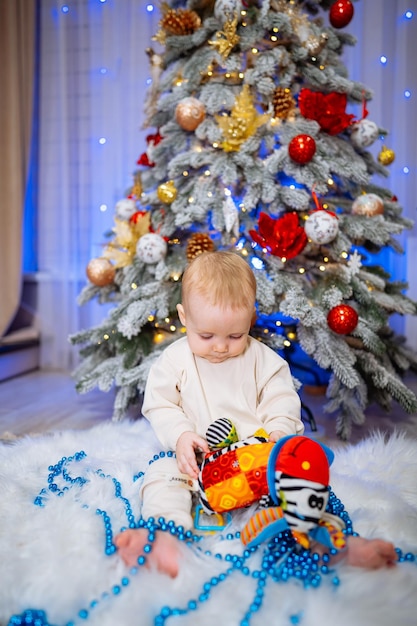 Kleines Kind spielt mit einem Spielzeug auf dem Hintergrund eines Weihnachtsbaums