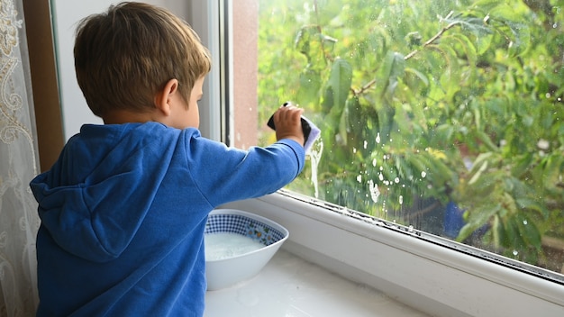 Kleines Kind wäscht das Fenster. Foto in hoher Qualität