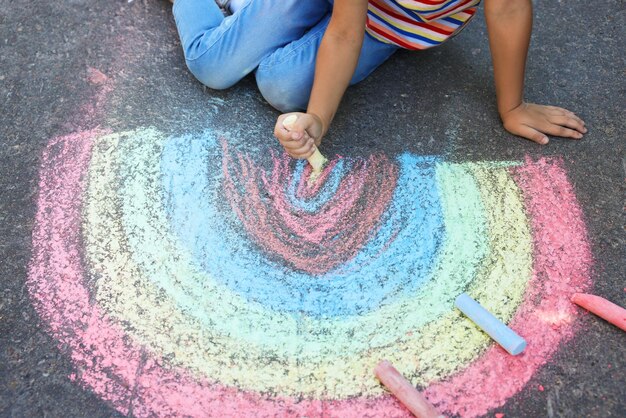 Foto kleines kind zeichnet regenbogen mit bunter kreide auf asphalt in der nähe