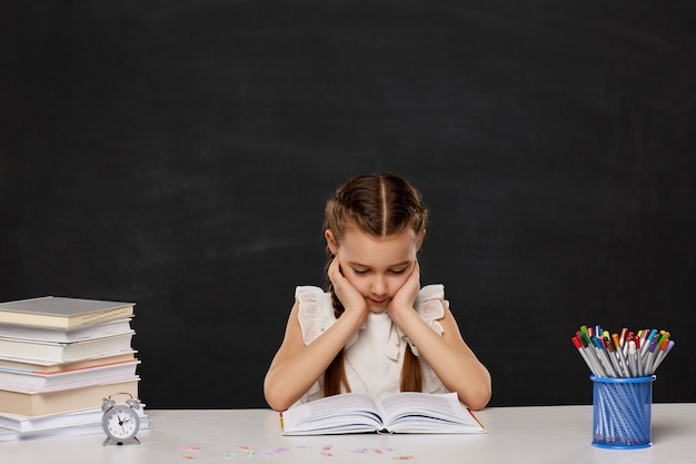 Kleines Kindermädchen, das ein Buch im Klassenzimmer liest