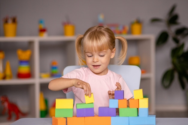 Kleines Kindermädchen, das Holzspielzeug zu Hause oder im Kindergarten spielt