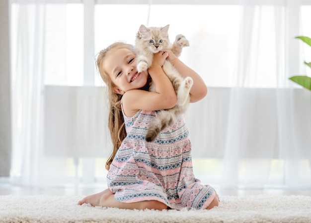 Kleines Kindermädchen, das Ragdollkätzchen hält und es streichelt. Hübsches weibliches Kind glücklich mit katzenartigem Kätzchenhaustier zu Hause