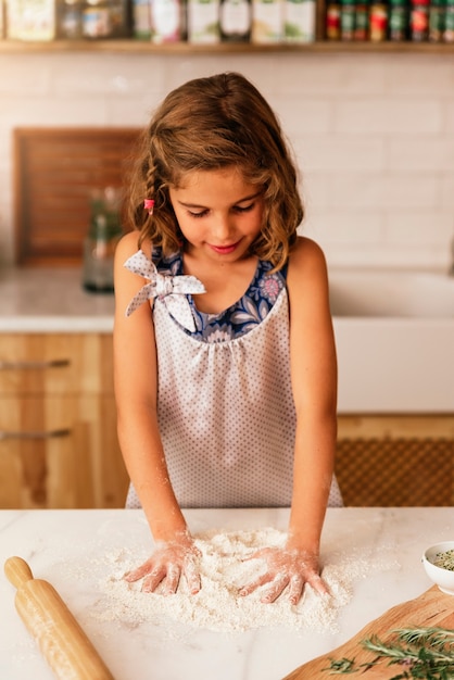 Kleines Kindermädchen, das Teig knetet, bereiten sich zum Backen von Keksen vor. Konzept des Säuglingskochs.
