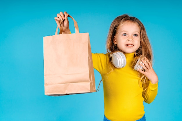 Kleines Kindermädchen halten Papiertüte lokalisiert auf blauem Hintergrund