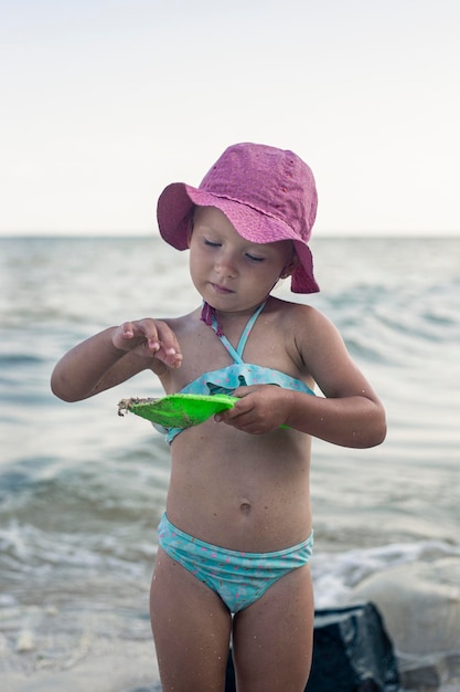 Kleines Kindermädchen in einem Badeanzug, in einem Panama, spielt in der Nähe des Meeres.