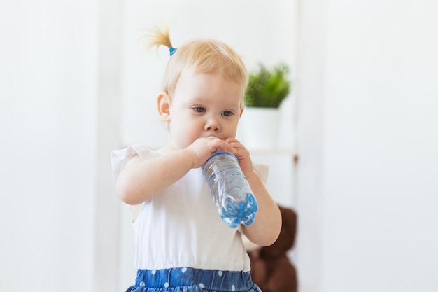 Kleines Kleinkind-Baby mit einer Flasche Mineralwasser zu Hause. Kinder- und Familienkonzept.