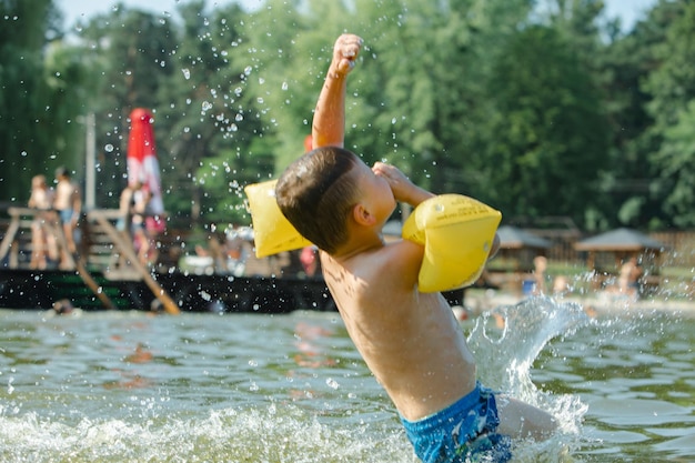 Kleines Kleinkind, das im See mit aufblasbaren Armhilfen schwimmt, unterstützt den Sommersee