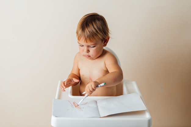 Kleines Kleinkindbaby spielt mit den Filzstiften und zeichnet bunte Linien auf Papier